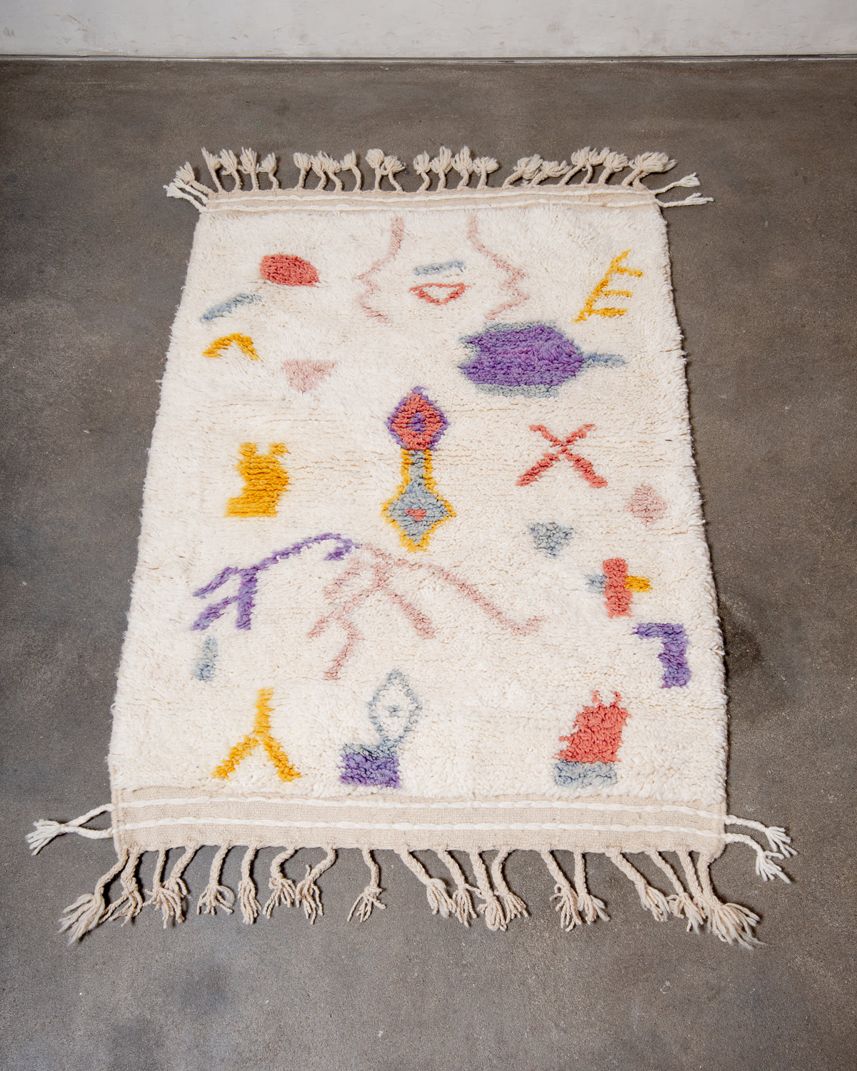Berberlin Special Edition Beniourain rug made of cream wool with pastel coloured abstract design laying on concrete floor.
